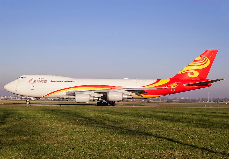 Suparna Airlines Boeing 737 parked on grass, showing the carrier's signature red tail. 