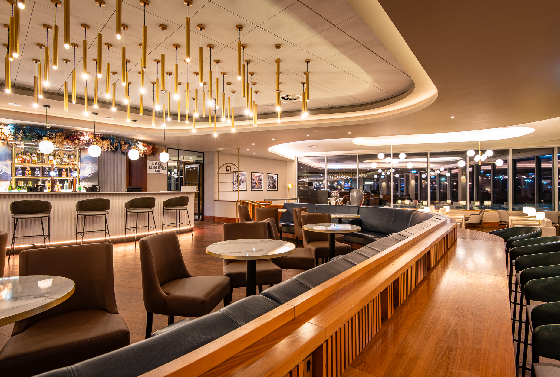 A premium airport lounge at night, with many lights hanging from the cieling and wooden accents to the furniture.