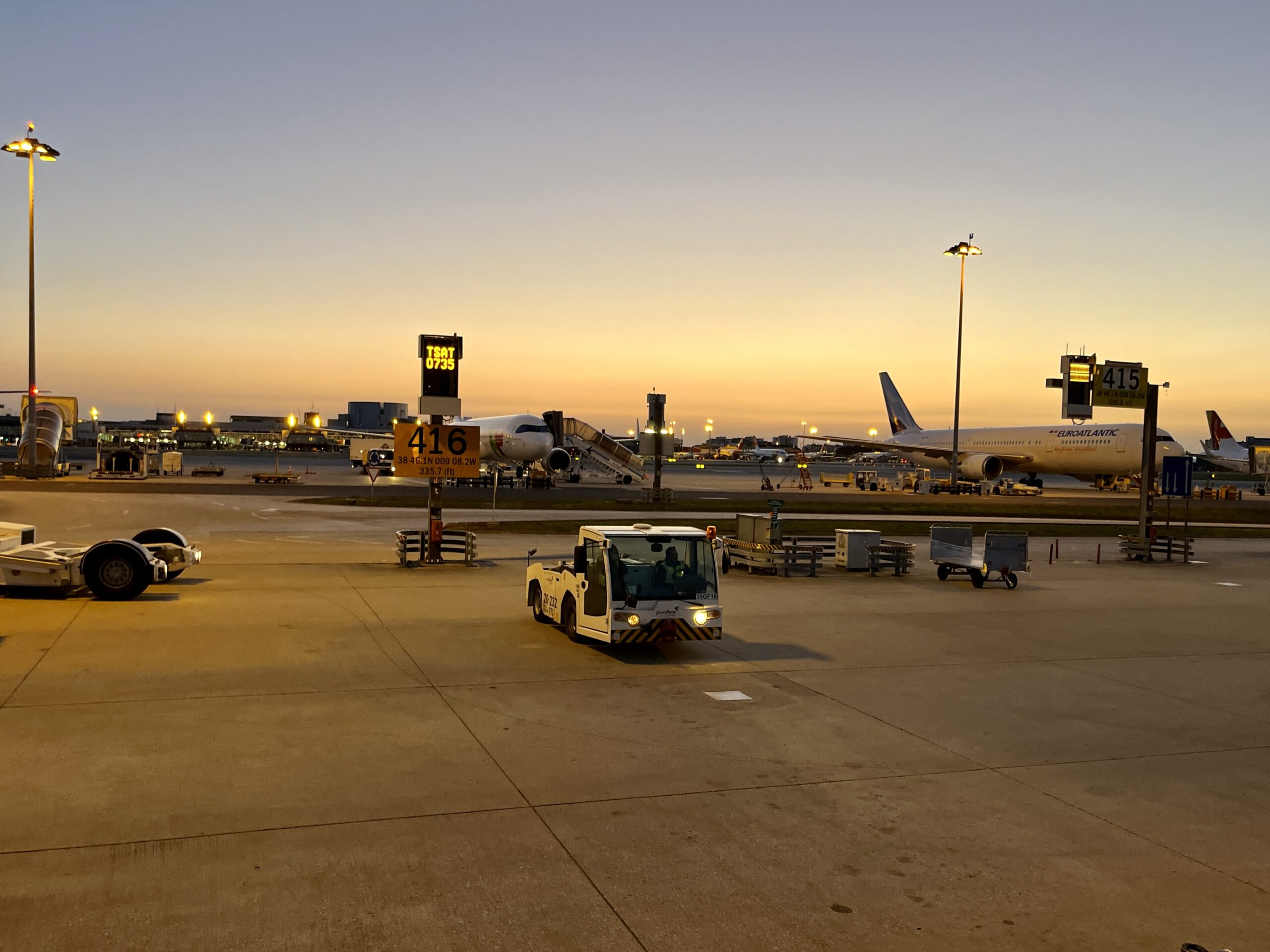 Sunrise at the airport tarmac. Some aircrafts and ground vehicles can be seen.