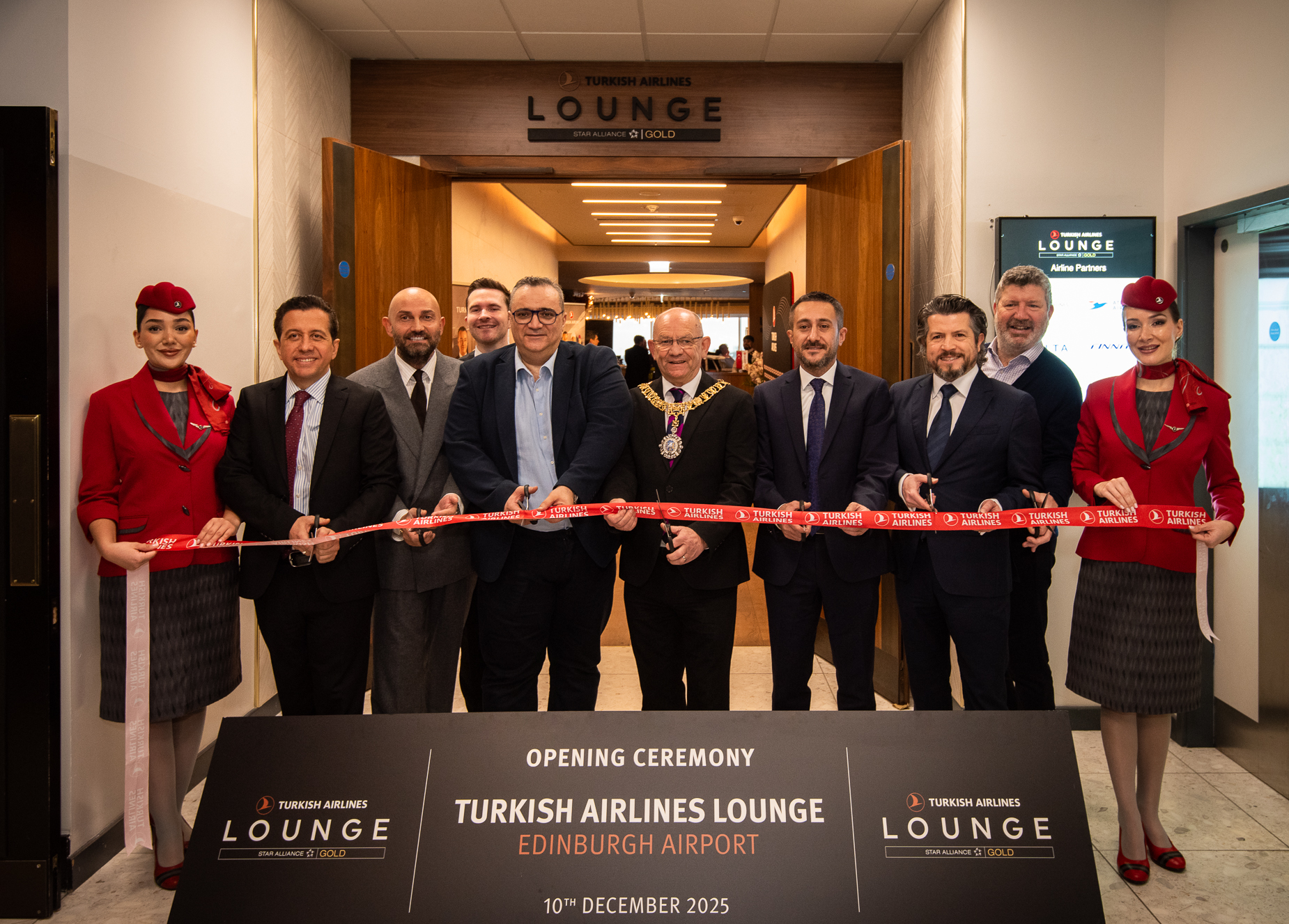 Multiple people stand in front of a Turkish Airlines ribbon with scissors, as two Turkish Airlines flight attendants hold the ribbon at either side.