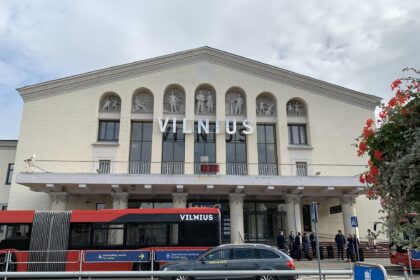 The front of the Vilnius Airport building's entrance with a bus and a car passing through.