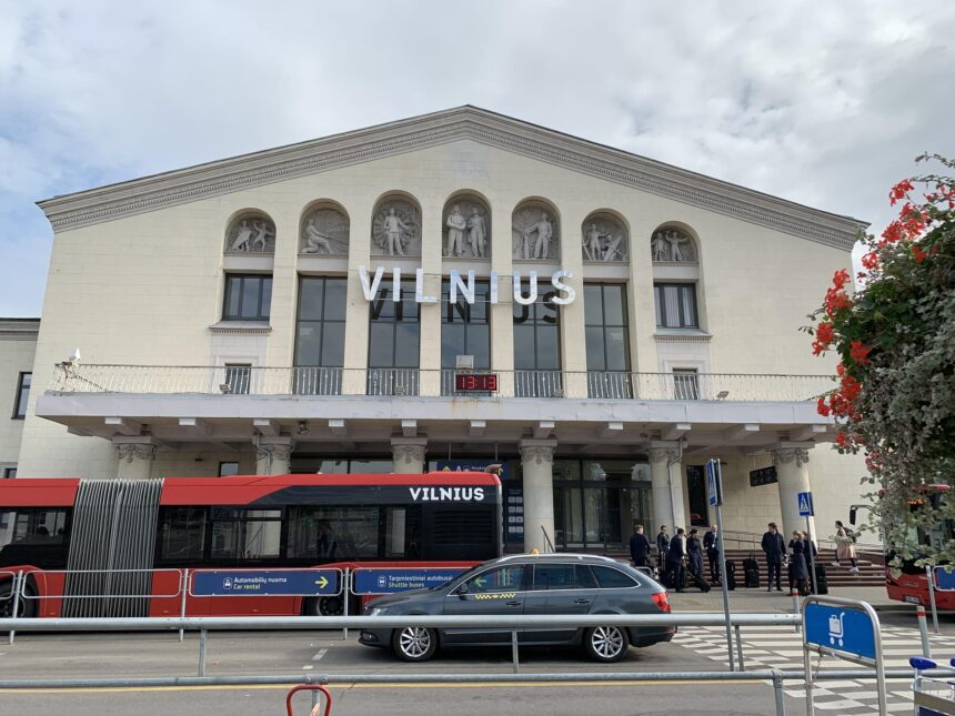 The front of the Vilnius Airport building's entrance with a bus and a car passing through.