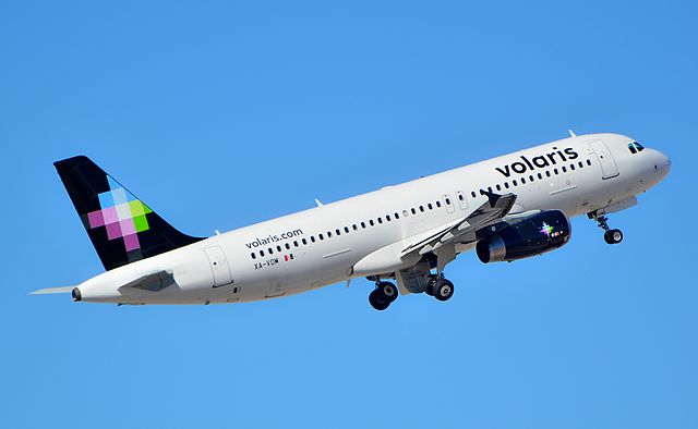 Volaris Airbus A320 in flight with its black tailed livery, against a blue sky.