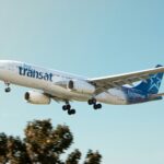 Air Transat aircraft flying in the blue sky. Trees in the background.