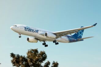 Air Transat aircraft flying in the blue sky. Trees in the background.