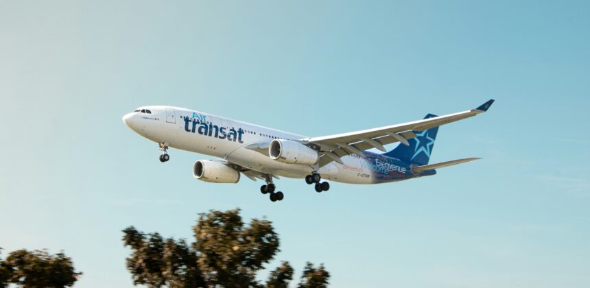 Air Transat aircraft flying in the blue sky. Trees in the background.
