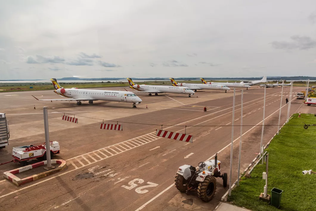 A series of Uganda Airlines planes docked at an airport, with a white tractor on the opposite side.