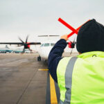 A ground crew worker in a high-visibility jacket guides a turboprop aircraft on the apron at Coventry Airport.