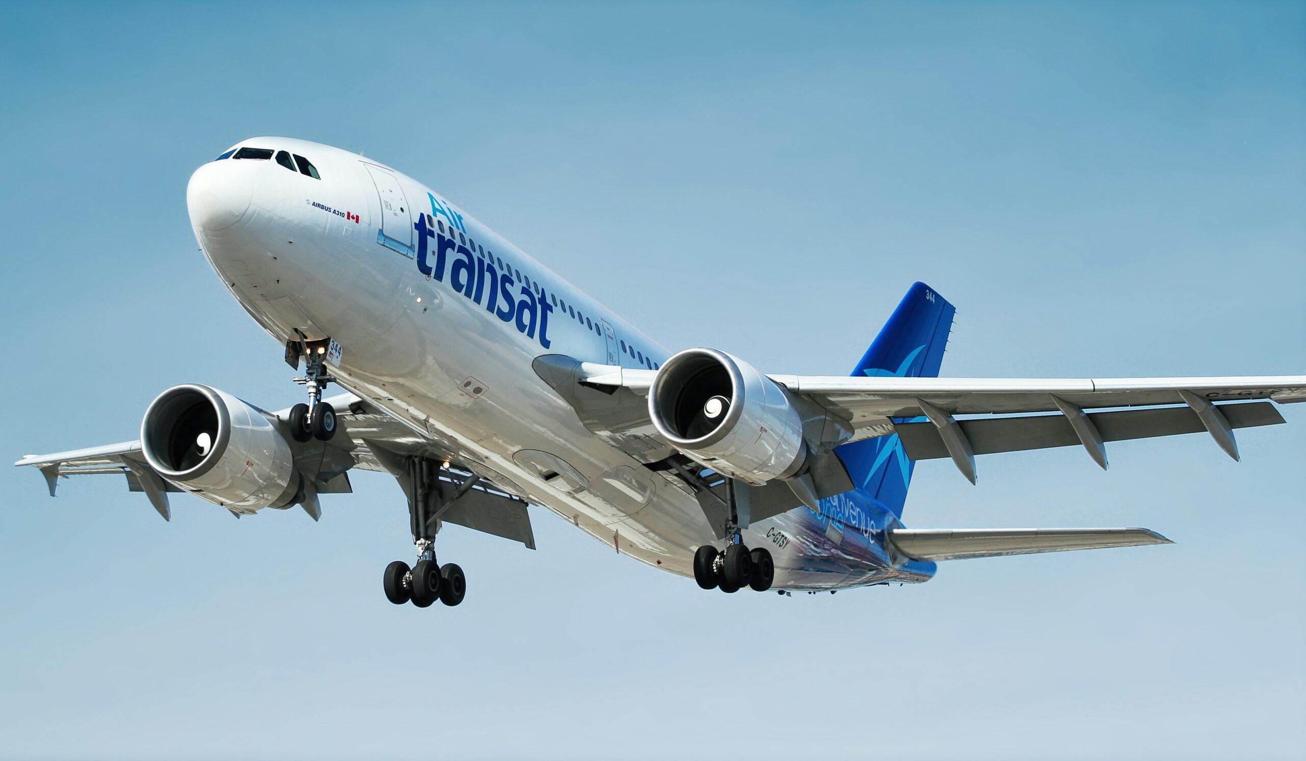 Air Transat Airbus A310, taking off, flying against a blue sky. White and blue livery, with the landing gear still out.