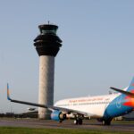 A Jet2 Aircraft taxis on the runway next to the control tower of Manchester Airport.