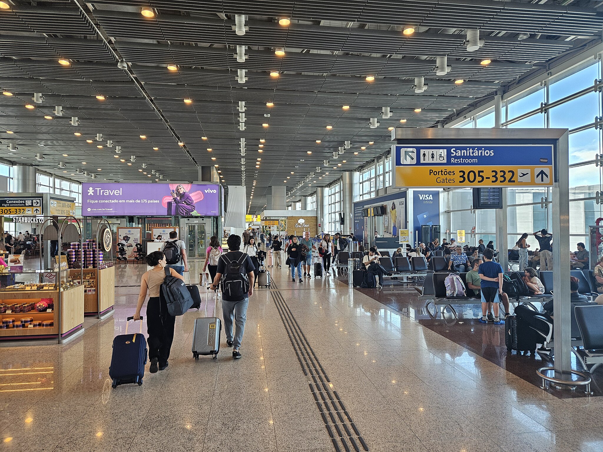 Departure lounge of Terminal 3 of Sao Paulo Guarulhos International Airport, with shops and people waiting in seats lining either side of the hall.