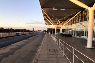 Side view of London Stansted Airport exterior, railings in front of the building, blue sky in background.