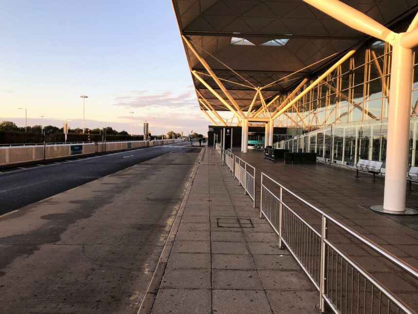 Side view of London Stansted Airport exterior, railings in front of the building, blue sky in background.