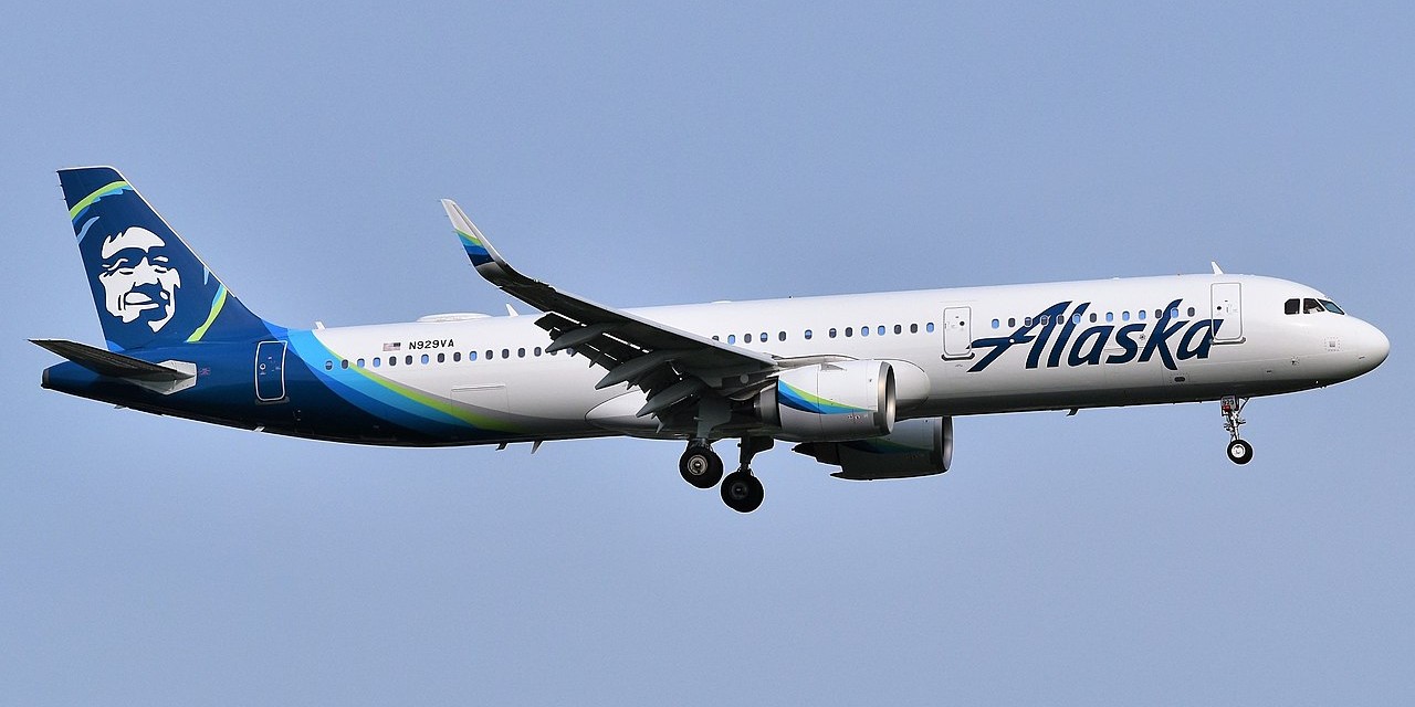 Alaska Airlines aircraft flying in the blue sky.