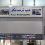 Arrivals area at Aleppo Airport, with signage written in English and Arabic.