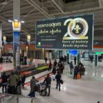 Departure screen at Tbilisi airport, passengers collecting their bags.