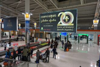 Departure screen at Tbilisi airport, passengers collecting their bags.