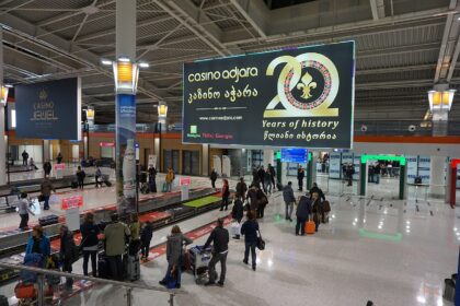 Departure screen at Tbilisi airport, passengers collecting their bags.
