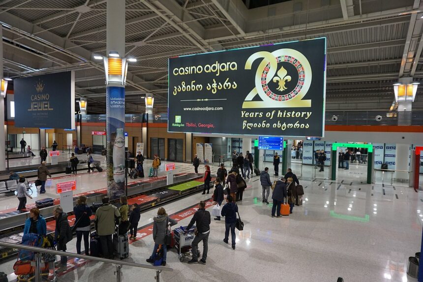 Departure screen at Tbilisi airport, passengers collecting their bags.