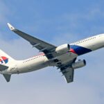 A low-angle shot of a Malaysia Airlines Boeing 737-800 aircraft climbing into a slightly cloudy blue sky. The plane is white with the signature red and blue airline livery and logo on the tail. The registration number "9M-MSE" is visible on the rear fuselage and under the wing. The landing gear is retracted, and the winglets feature the airline's logo.