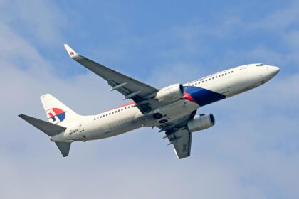 A low-angle shot of a Malaysia Airlines Boeing 737-800 aircraft climbing into a slightly cloudy blue sky. The plane is white with the signature red and blue airline livery and logo on the tail. The registration number "9M-MSE" is visible on the rear fuselage and under the wing. The landing gear is retracted, and the winglets feature the airline's logo.