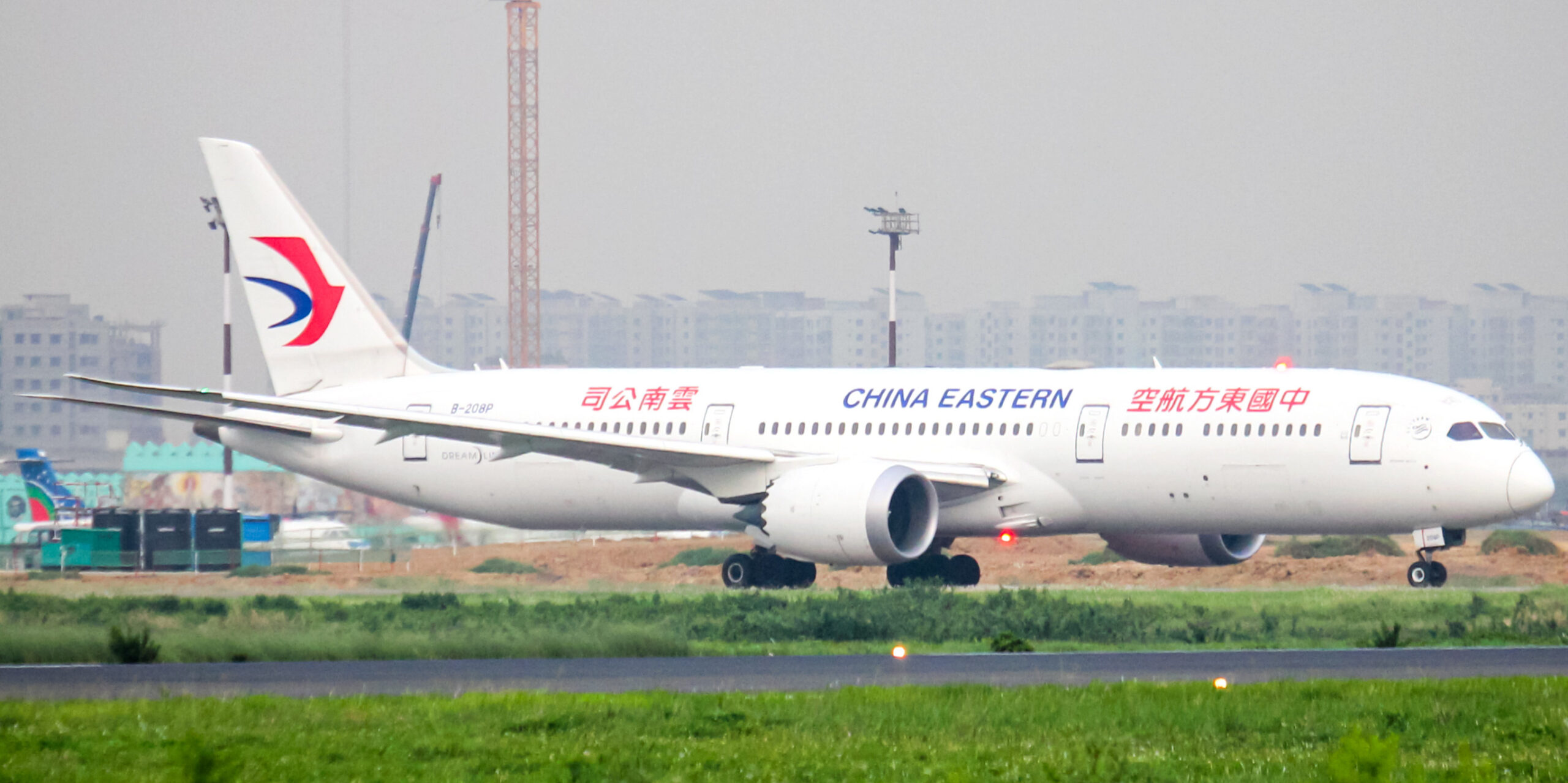 A white China Eastern Airlines Boeing 787 Dreamliner on a runway with a city skyline in the background.