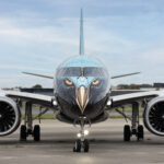 A front-on view of an Embraer E195-E2 commercial aircraft parked on a tarmac. The nose of the plane features a highly detailed "Tech Eagle" livery, with stylised eagle eyes and a beak painted over the cockpit and nose cone.