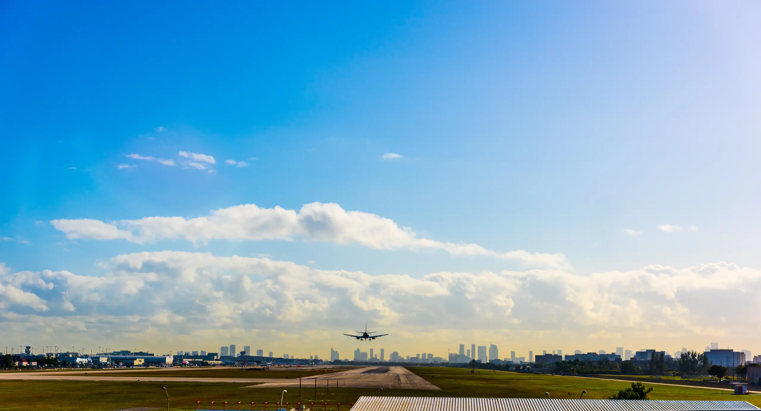 View of aircraft landing on Miami runway, blue sky with clouds in the background.
