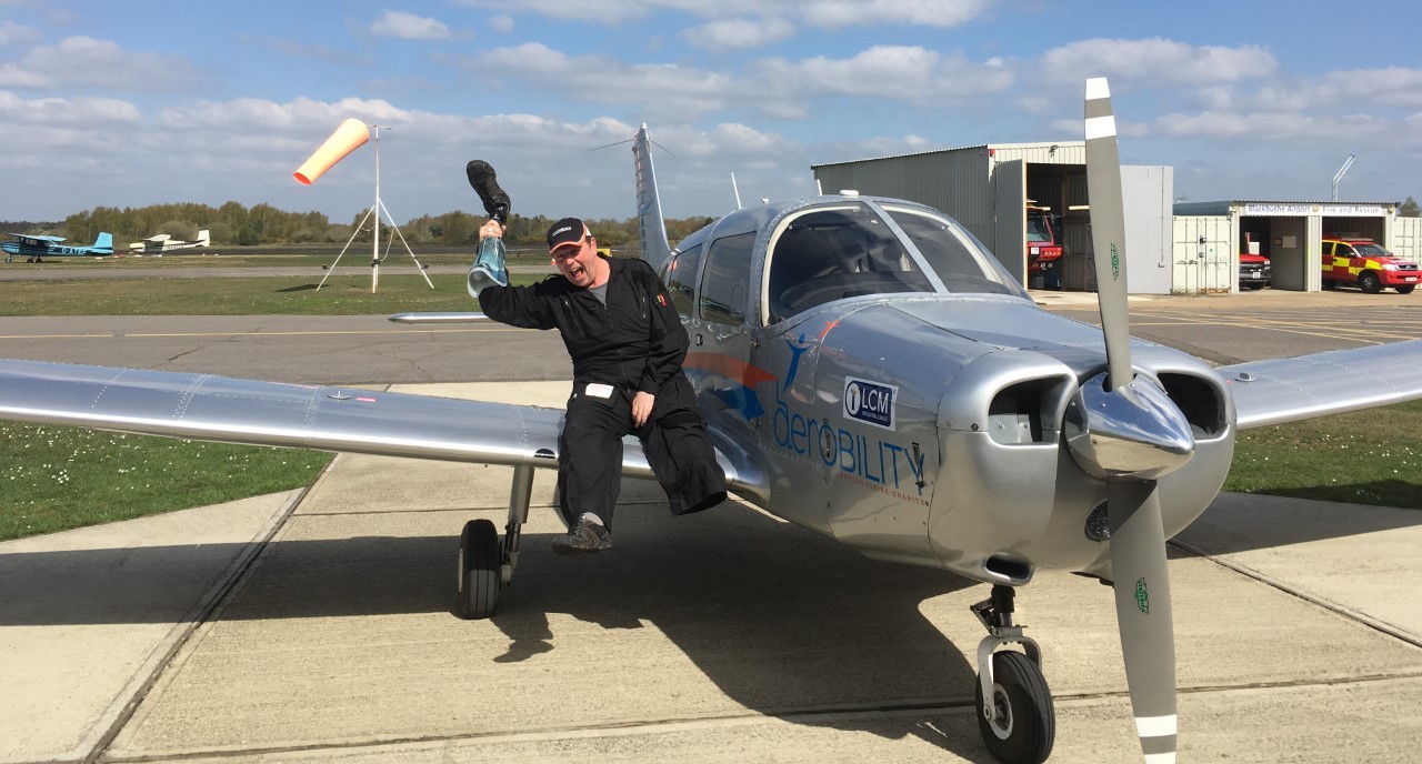 Neil Tucker, sitting on the wing of an aircraft, holding his prosthetic leg.