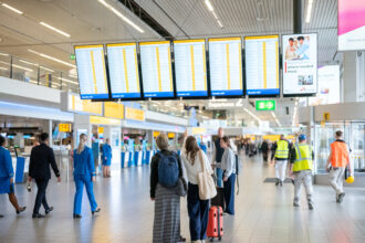 Amsterdam Airport Schiphol departure hall. Passengers carry suitcases and look at the gate screens.