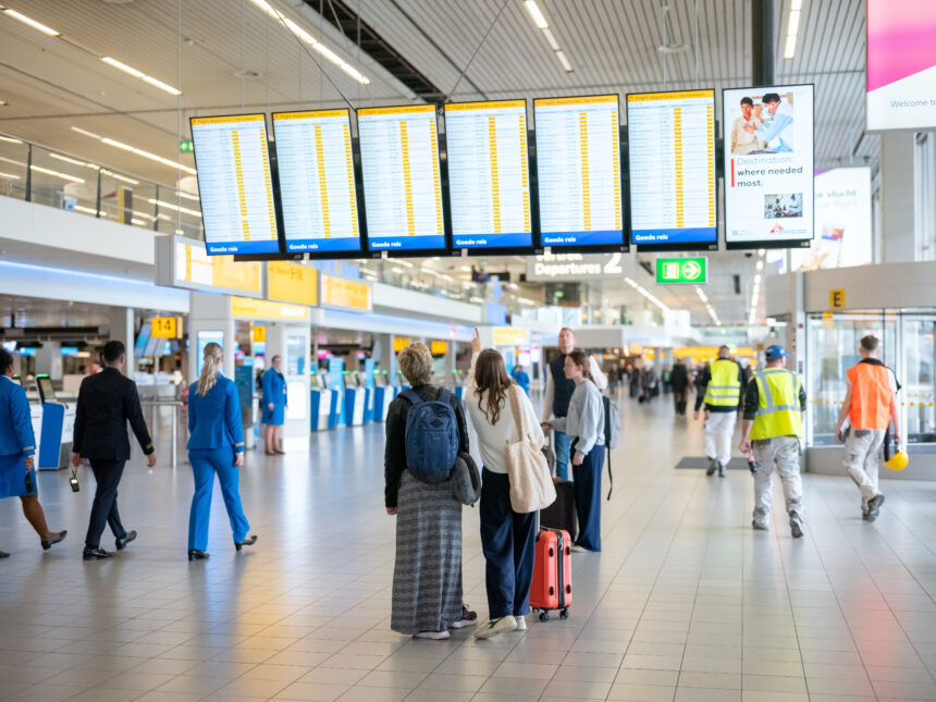 Amsterdam Airport Schiphol departure hall. Passengers carry suitcases and look at the gate screens.