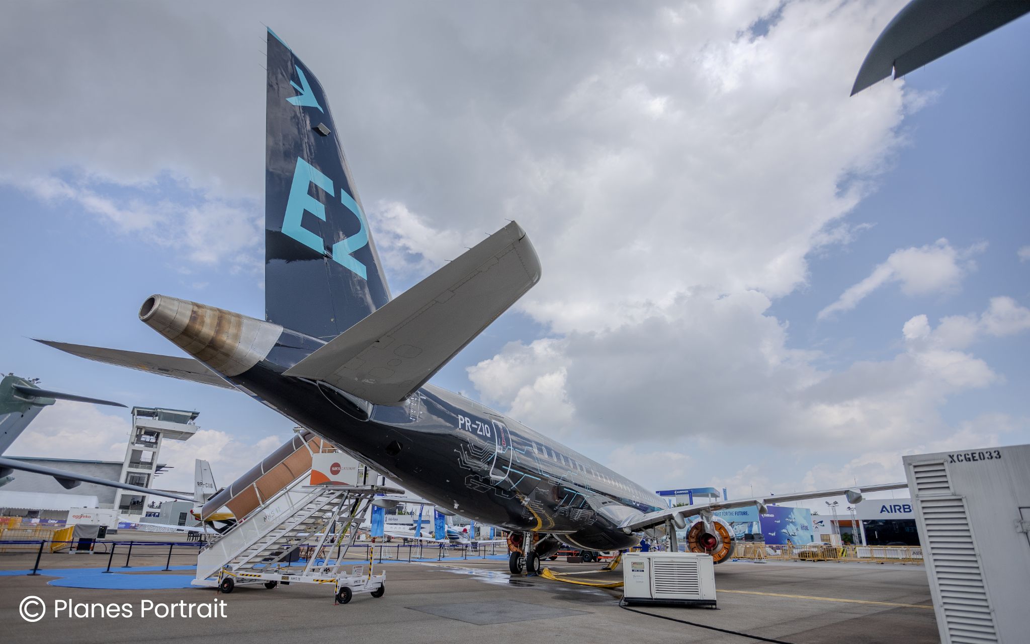 A low-angle rear view of a black Embraer E2 jet at the Singapore Airshow. The large vertical stabilizer features a bright blue 
