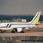 A Sudan Airways Airbus A310-300 sits on an airport tarmac. The plane features a white fuselage with blue and yellow stripes and Arabic calligraphy on the tail.