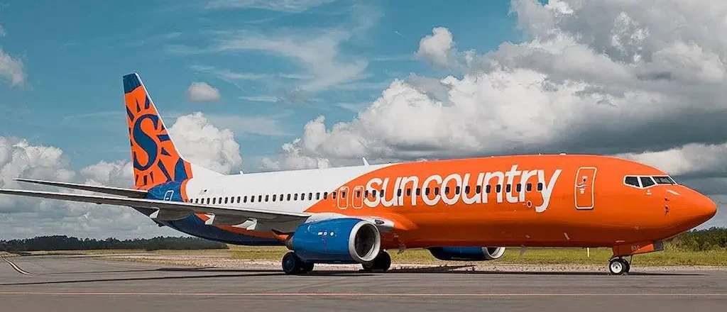 A Sun Country Airlines Boeing 737 sits on the tarmac, showing its orange, blue and white livery with the “S” logo on the tail.