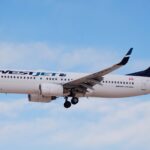 A WestJet 737 aircraft flies above clouds with landing gear engaged.