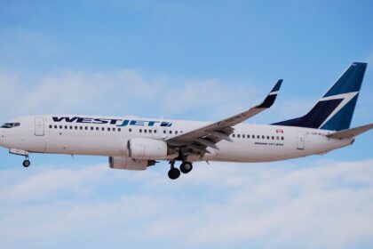 A WestJet 737 aircraft flies above clouds with landing gear engaged.