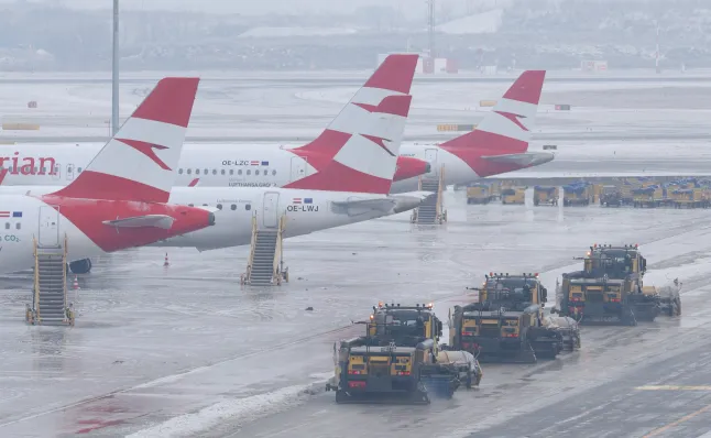 Planes parked on icy runways at Vienna International Airport, operations halted as thick ice repeatedly refreezes despite clearing efforts.