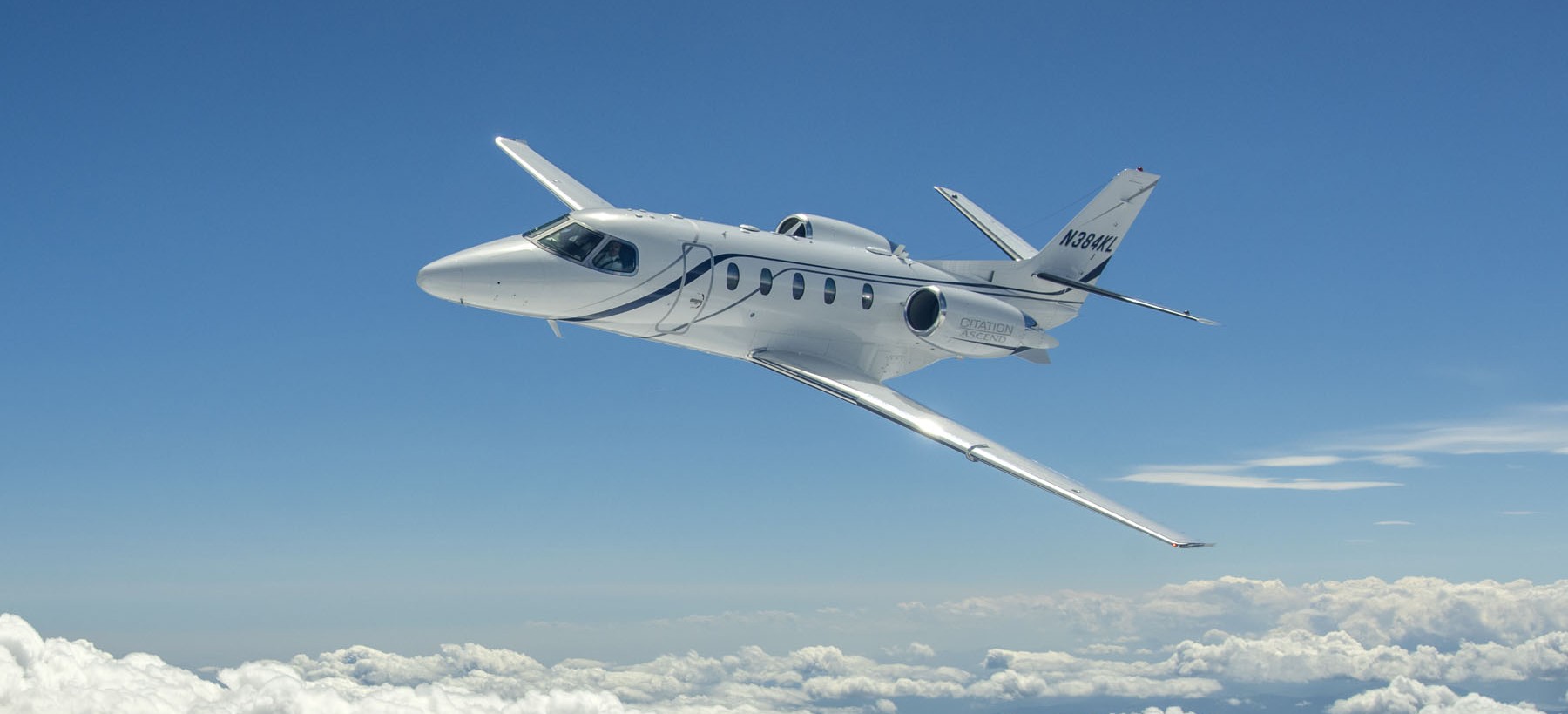 Citation Ascend business jet flying above the clouds in blue sky.