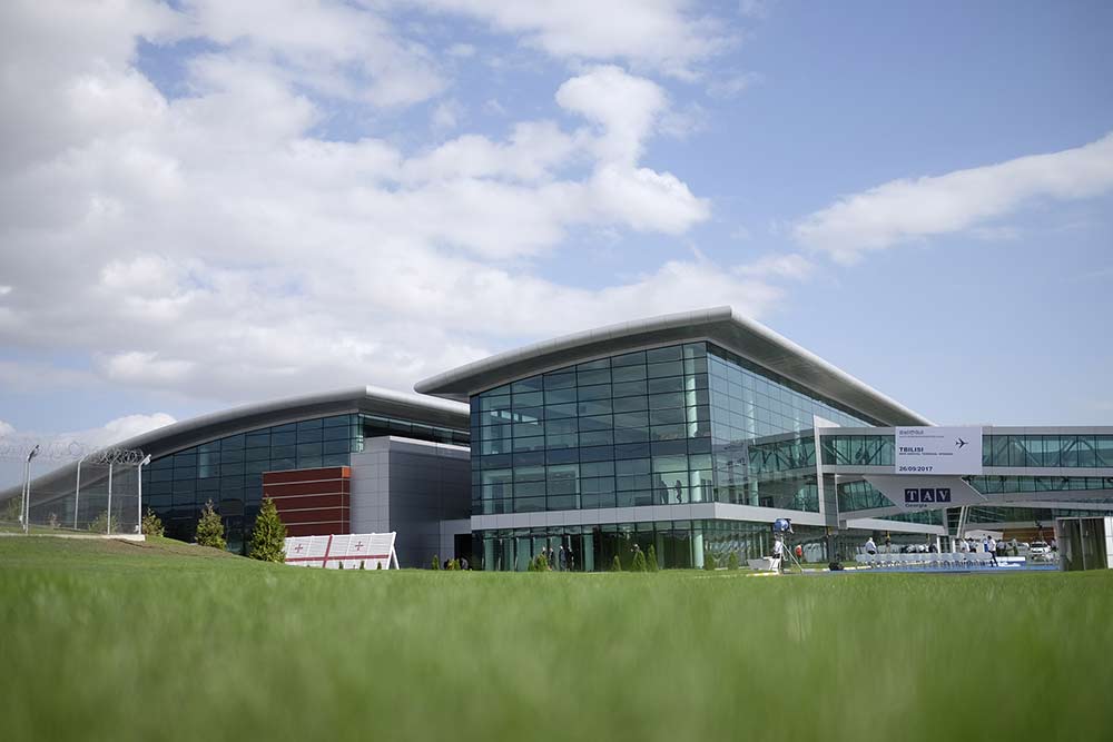 View of Tbilisi Airport from outside, grass in foreground, blue sky in background.
