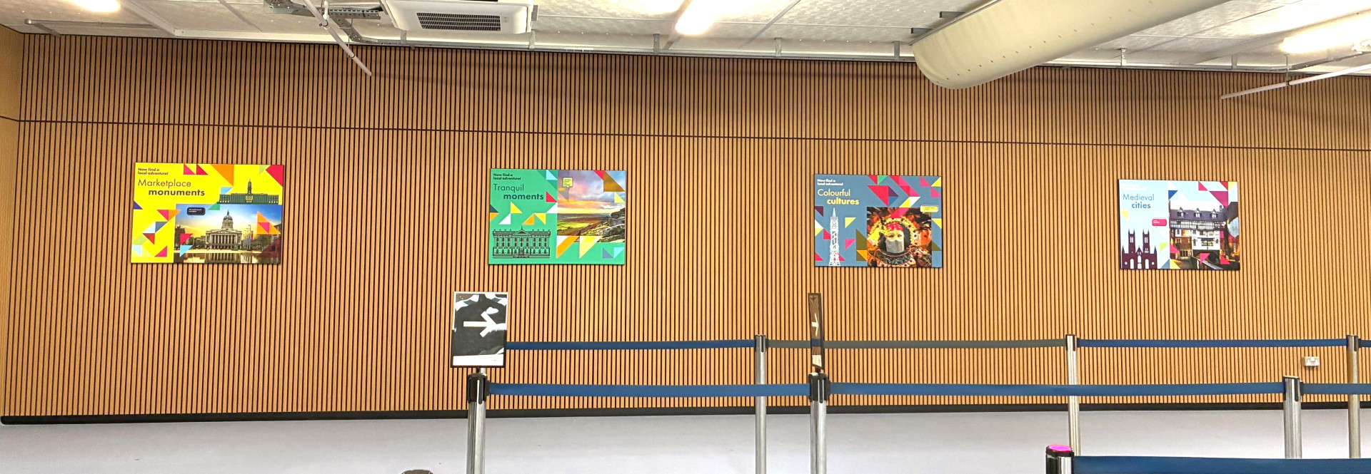 Arrival hall at the East Midlands Airport, wooden panel, four posters on the wall.