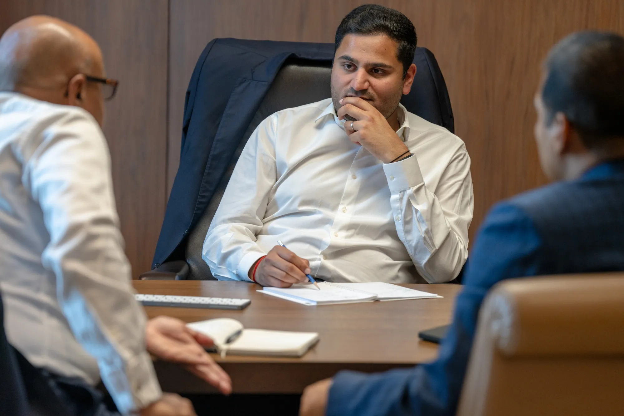 A stocky man in a boardroom talking to two of his representatives