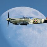 Spitfire flying in the sky, directly in front of the moon, blue skies.