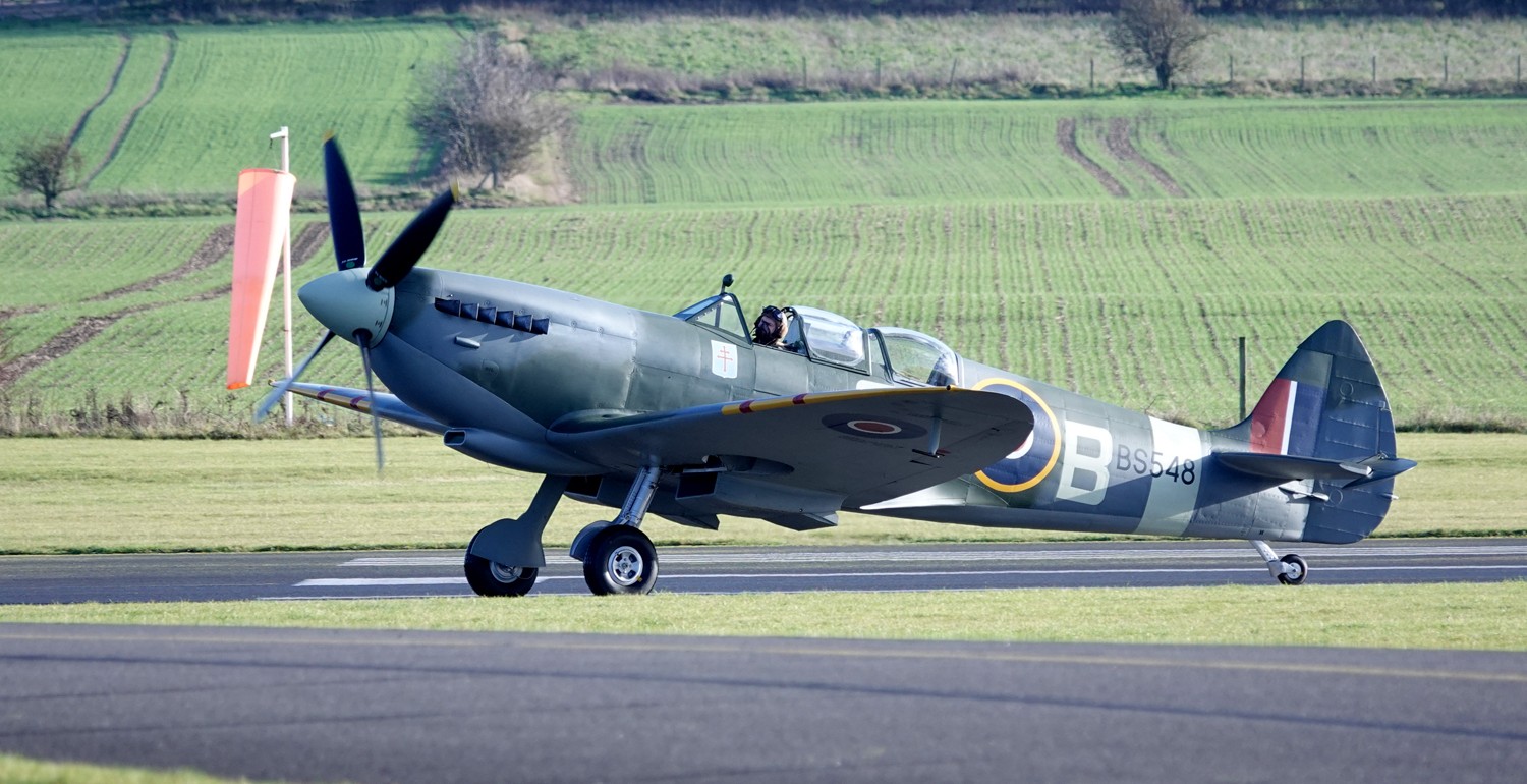 Supermarine Spitfire on the tarmac before takeoff, trees and grass in the background.