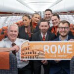 An easyJet crew aboard an aircraft celebrate the inaugural Glasgow-Rome flight with a sign reading "Glasgow Airport to Rome".