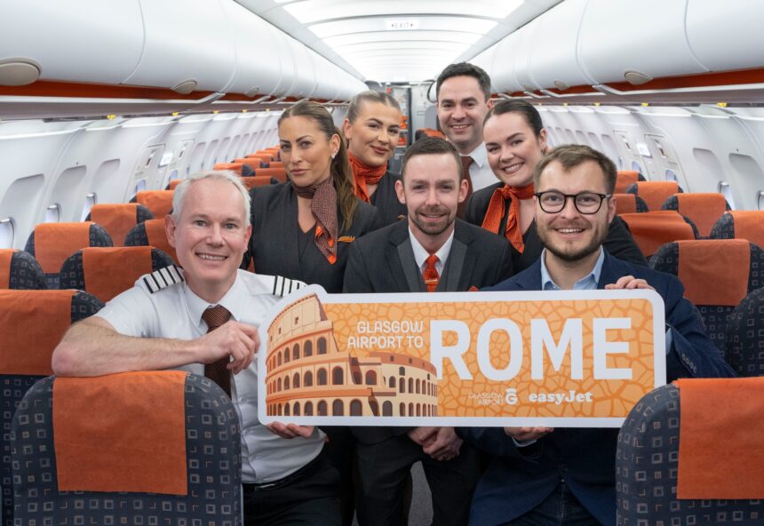 An easyJet crew aboard an aircraft celebrate the inaugural Glasgow-Rome flight with a sign reading "Glasgow Airport to Rome".