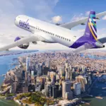 Avelo Airlines aircraft, flying over a city, blue sky.