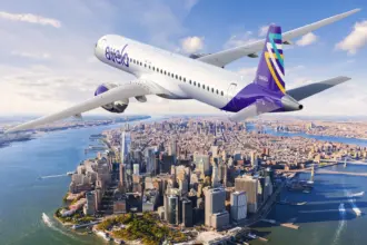 Avelo Airlines aircraft, flying over a city, blue sky.