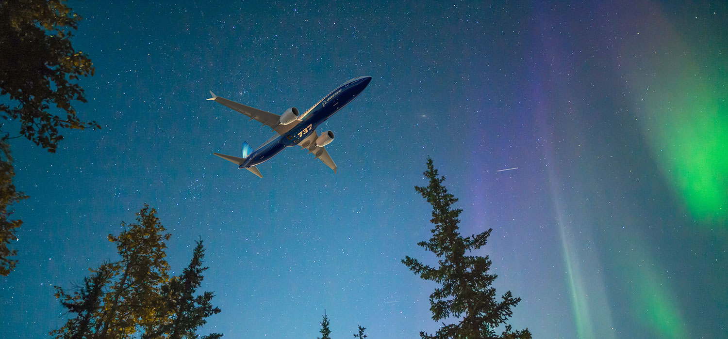Boeing 737 MAX aircraft flying in the night, northern lights in the background.