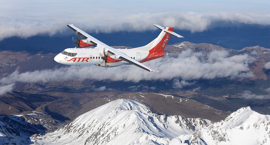 ATR 42-600 aircraft in its new red and white livery, flying over snowy mountains.
