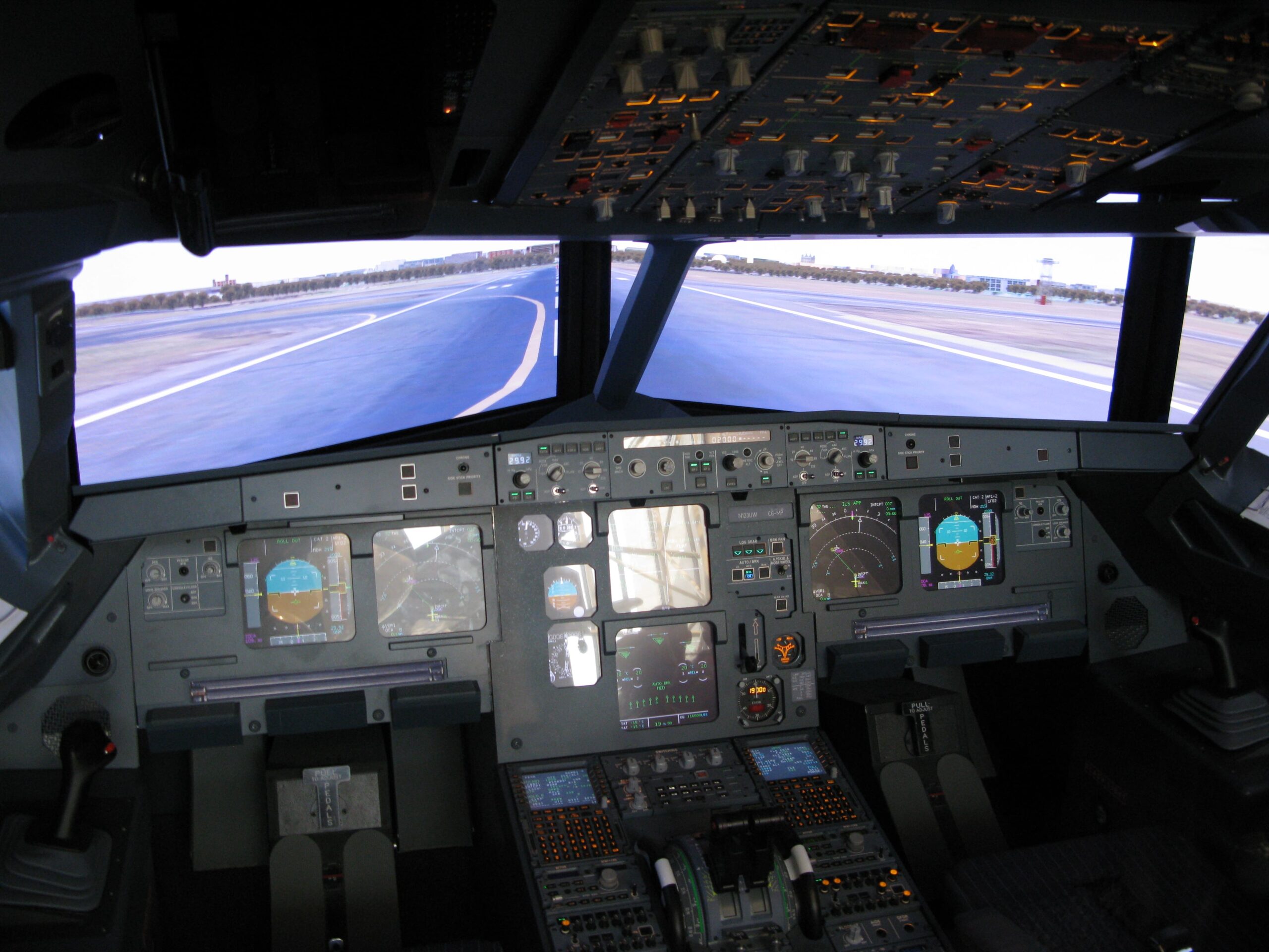 Cockpit of the simulator for an Airbus A320 family aircraft. No pilots in the photo. Flight instruments are visible. Simulated runway also visible through the windows.